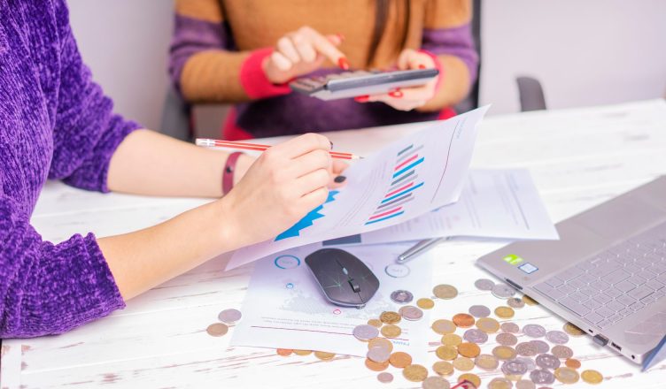 Two women analyzing financial charts with a laptop and coins on desk in an office setting. — 4 amazing Forex career for the r