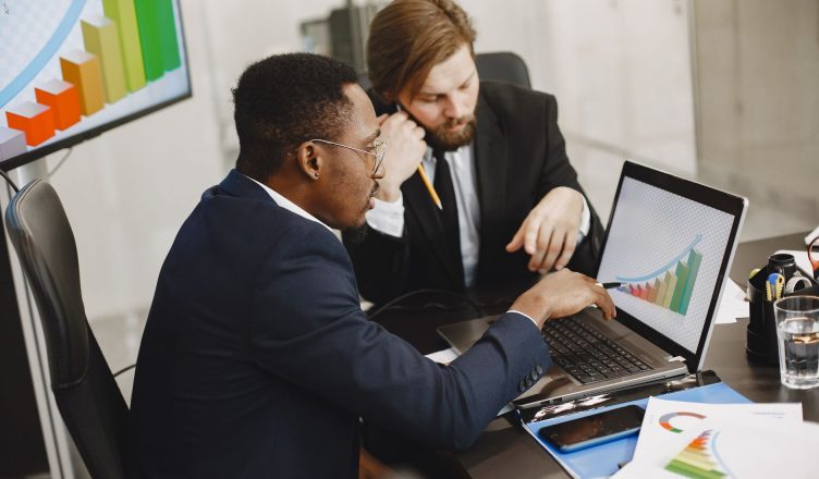 Two business professionals working on growth charts using laptop in an office setting. — 5 Advantages of having a Demat Accou
