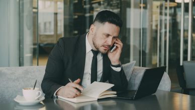 Businessman talks on phone while writing notes in a modern cafe. — A complete step-by-step guide to make an effective resume!