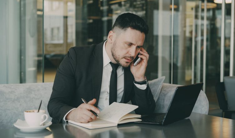 Businessman talks on phone while writing notes in a modern cafe. — A complete step-by-step guide to make an effective resume!