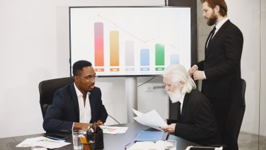 Three businessmen discussing financial data in a modern office setting with charts. — A Quick Overview On Shooting Strategy o