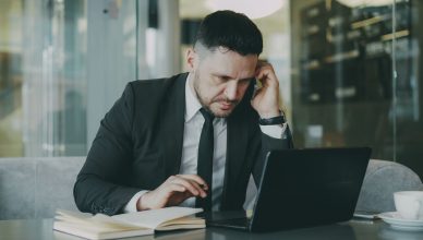 Focused businessman in suit multitasking on phone and laptop in modern office. — All you need to know about Dropshipping and