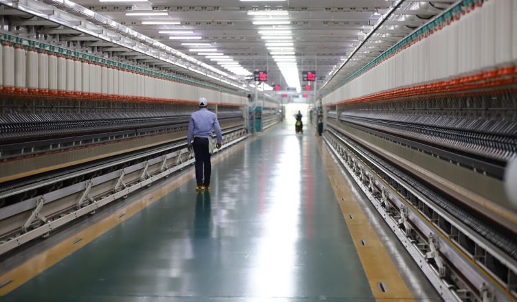 A man walks through a well-lit hallway in a modern industrial textile plant in India. — All you need to know about Fume Extra