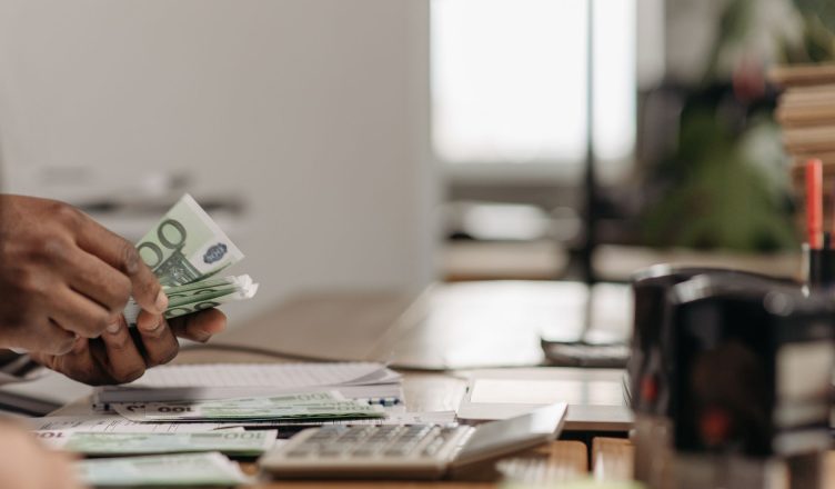 Close-up of hands counting euro bills at an office desk with a calculator. — Being a successful share trader