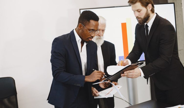 Three businessmen engaged in document signing in a modern office setting. — Benefits Of Having Cpa Services In Portland