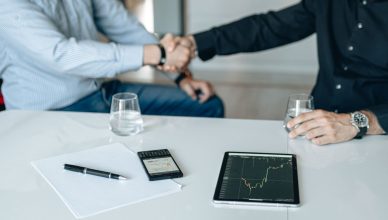 Business meeting with handshake and financial analysis displayed on a tablet. — Best Side Hustles That Can Help You Earn Easy
