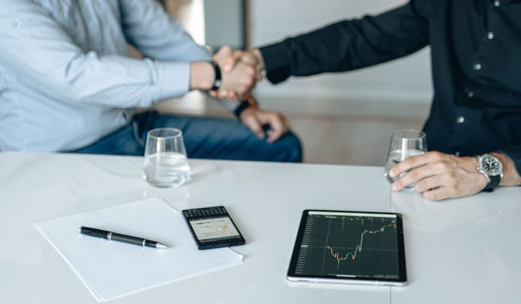 Business meeting with handshake and financial analysis displayed on a tablet. — Best Side Hustles That Can Help You Earn Easy