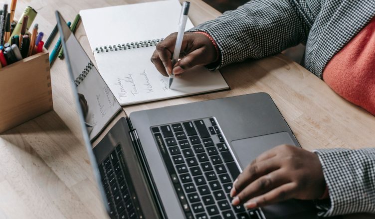 Crop unrecognizable African American female in formal wear writing notes in notepad while working on laptop — Buff Away Dead