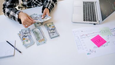 Person counting cash next to laptop and stock market charts on a white table. — Buy low and benefit from falling markets with