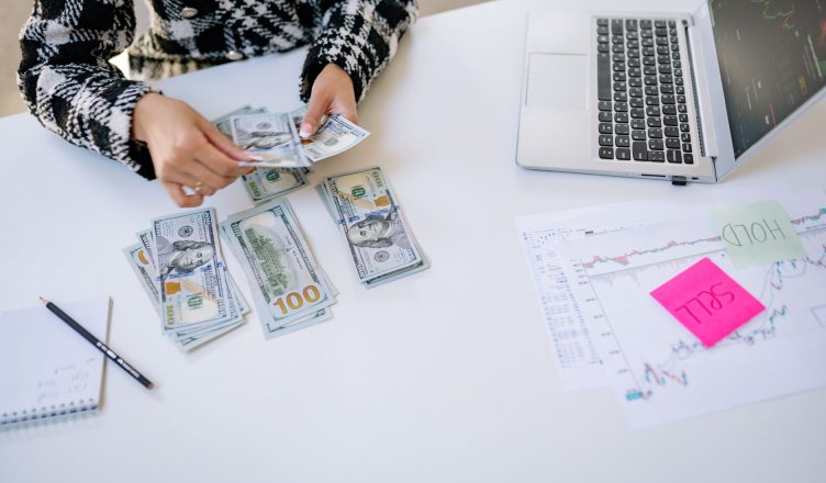 Person counting cash next to laptop and stock market charts on a white table. — Buy low and benefit from falling markets with