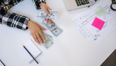 Businesswoman counting dollar bills with financial charts and laptop on table. Investment and finance concept. — Efficient ma