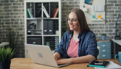 Cheerful woman working on laptop in modern office setting with smartphone and notebook. — Essential Tips On How To Create A B