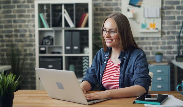 Cheerful woman working on laptop in modern office setting with smartphone and notebook. — Essential Tips On How To Create A B