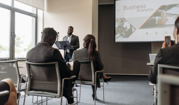 A business professional delivering a presentation in a conference room with diverse attendees. — Frequently Asked Questions R