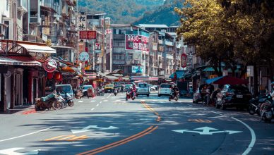 Vibrant urban street scene with shops, vehicles, and mountains in an Asian city. — Here's What You Need To Know About The Lat