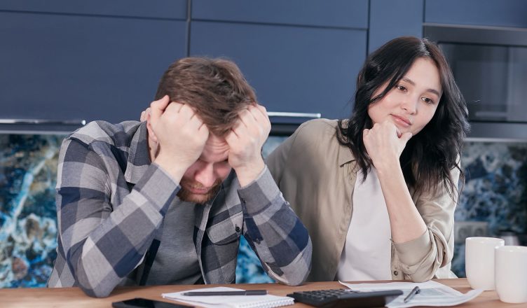 A couple looking worried while reviewing financial documents at a kitchen table. — Home Loan Interest Rate