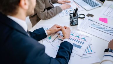 Business team analyzing financial graphs at a meeting table, fostering collaboration in an office environment. — How can you