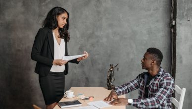 A formal office meeting between a woman and a man discussing documents. — How Long Does A Malpractice Lawsuit Take?