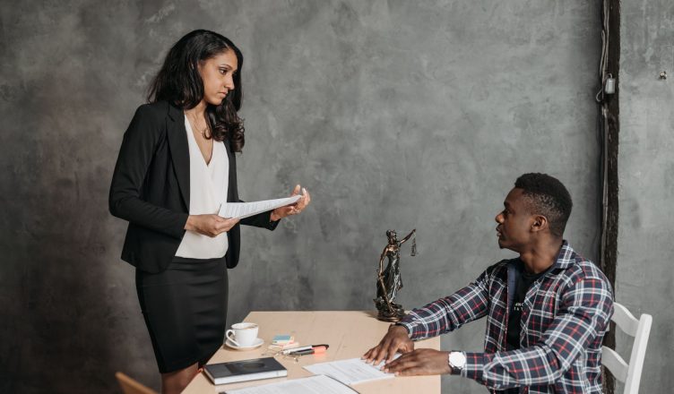 A formal office meeting between a woman and a man discussing documents. — How Long Does A Malpractice Lawsuit Take?