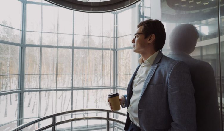 Businessman in blue suit with coffee cup looking out a large window, reflecting on a winter landscape. — How to ensure that y