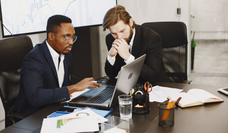 Two businessmen engaged in a strategy meeting with laptops and charts. — How to Find Your Dream Home