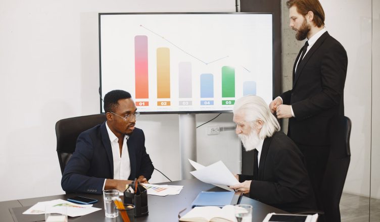 Three businessmen discussing financial data in a modern office setting with charts. — How to Guarantee the Success of Your Dr