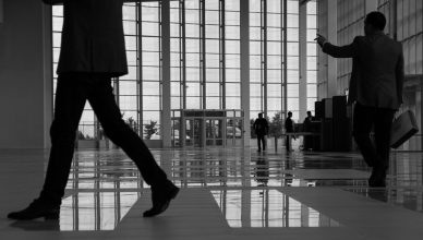 Business professionals walk through a modern, glass-paneled indoor space. — How to hire a qualified bodyguard in London?