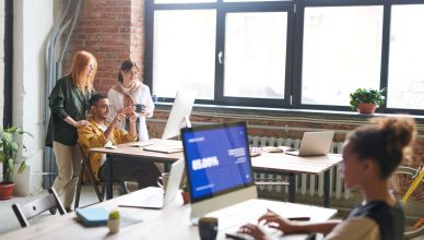Team discussing ideas in a modern office setting, enhancing work through digital devices. — How to Outsource SEO Services and