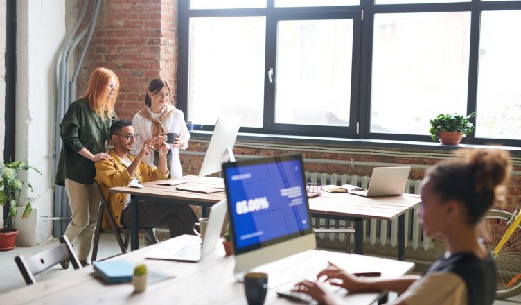 Team discussing ideas in a modern office setting, enhancing work through digital devices. — How to Outsource SEO Services and
