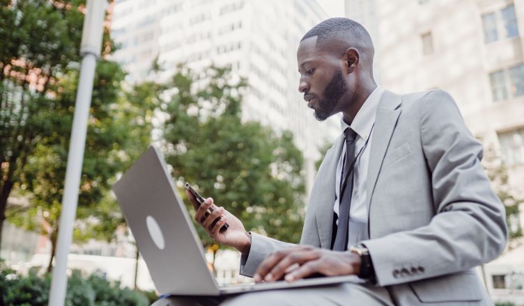 Businessman in a suit using a laptop and smartphone in an urban setting, blending technology with business. — Intra- day trad