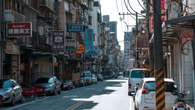 A busy street lined with cars and various colorful business signs on a sunny day. — Know about the competitors of amazon
