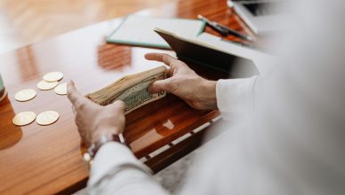 Person counting cash and coins on a wooden table, emphasizing financial tasks. — Learning to stop overtrading the market
