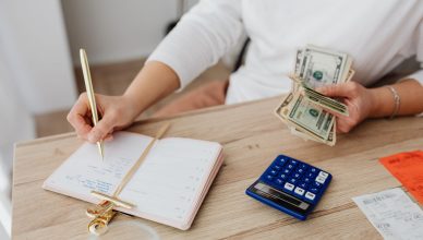 Adult holding cash and writing in planner while using a calculator at home. — Plus, points of buying the Tezos cryptocurrency