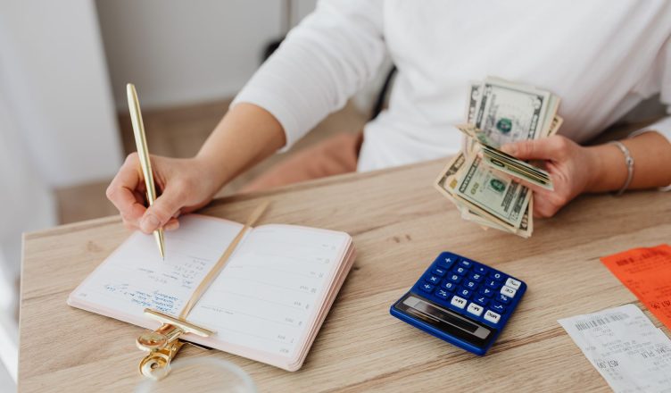 Adult holding cash and writing in planner while using a calculator at home. — Plus, points of buying the Tezos cryptocurrency