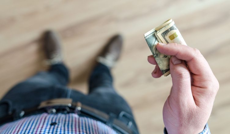 A person wearing denim and a checked shirt holds folded dollar bills in their hand indoors. — Repairing Your Credit after Ban