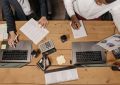 High-angle view of professionals working collaboratively with laptops and documents in an office. — Save More with H&M Promo