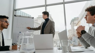 Professionals engaged in a collaborative business meeting with charts and laptops in a modern office setting. — Send items wi