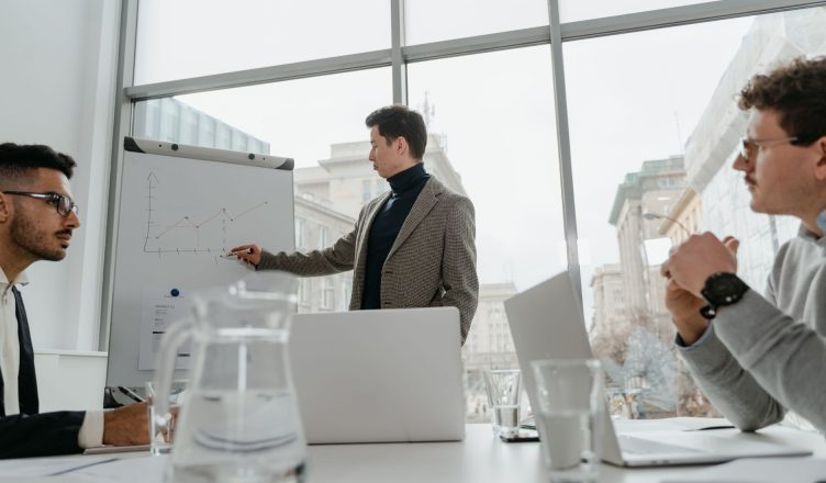 Professionals engaged in a collaborative business meeting with charts and laptops in a modern office setting. — Send items wi