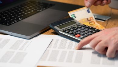 Close-up of hands using calculator with euro notes and laptop on desk. — Shopping on No Cost EMI - All you need to know