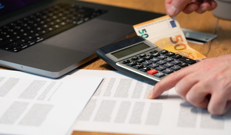 Close-up of hands using calculator with euro notes and laptop on desk. — Shopping on No Cost EMI - All you need to know