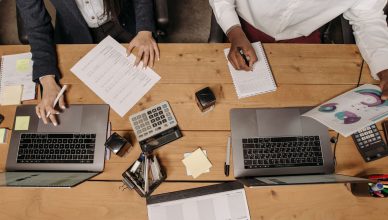 High-angle view of professionals working collaboratively with laptops and documents in an office. — SOME TIPS TO REDUCE RISKS