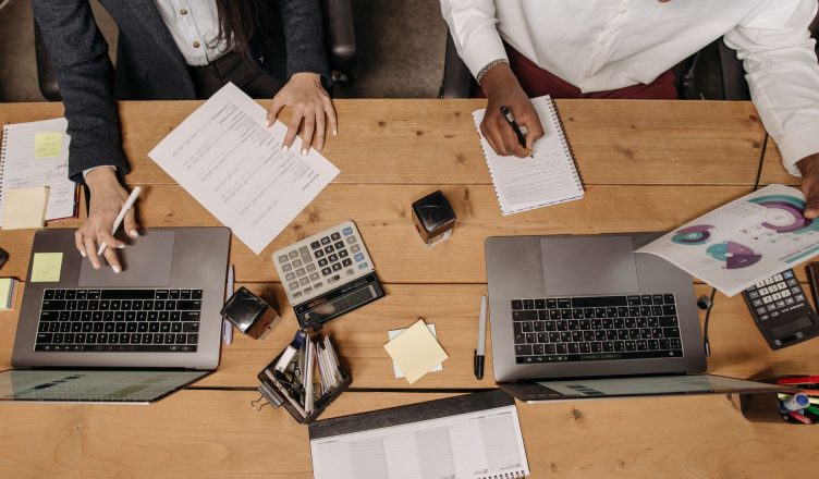 High-angle view of professionals working collaboratively with laptops and documents in an office. — SOME TIPS TO REDUCE RISKS