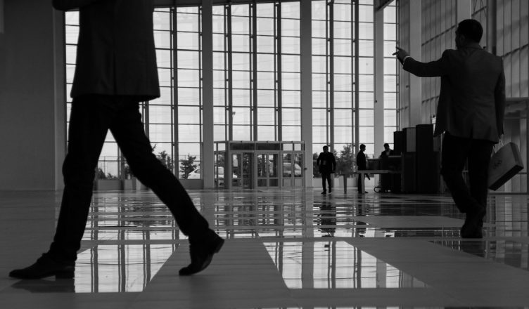 Business professionals walk through a modern, glass-paneled indoor space. — "Stay Ahead Anywhere with MT4 for Android Devices