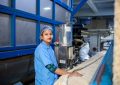 A woman in a blue uniform operates a machine in a textile factory, ensuring quality and precision. — How Containers A