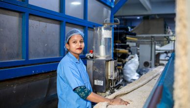A woman in a blue uniform operates a machine in a textile factory, ensuring quality and precision. — How Containers A