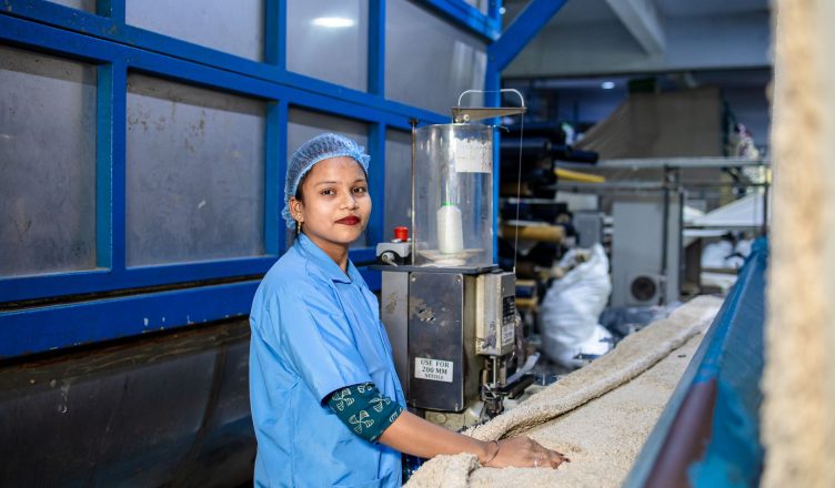 A woman in a blue uniform operates a machine in a textile factory, ensuring quality and precision. — How Containers A