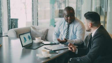 Two business professionals engaged in discussion over laptops and documents. — The Competition - How Does Your Brand