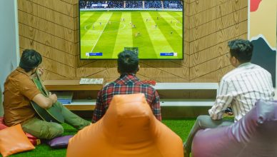 Three friends relaxing and playing a soccer video game indoors on a comfortable game night. — Unlock Unbelievable Rew