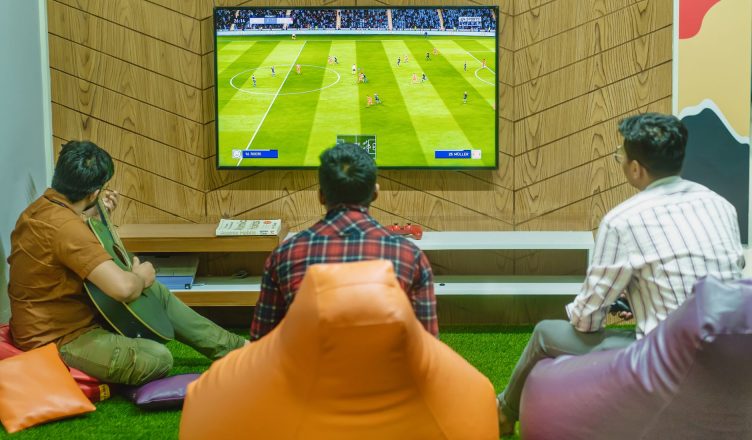Three friends relaxing and playing a soccer video game indoors on a comfortable game night. — Unlock Unbelievable Rew