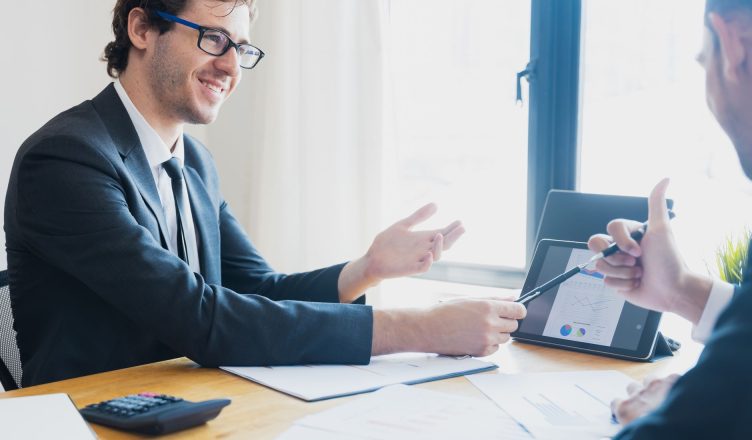 Two businessmen in formal attire discussing a business report in an office setting with a tablet. — SUCCESSFUL FOREX TRADING
